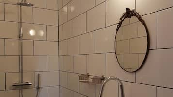 A modern bathroom with white tiles, a rectangular sink, a shower with a handheld showerhead, and a wall-mounted mirror.