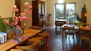 Een ruime eethoek met houten meubels, een grote houten tafel en stoelen. Er is een kast met glazen deuren en een vaas met bloemen op de tafel.