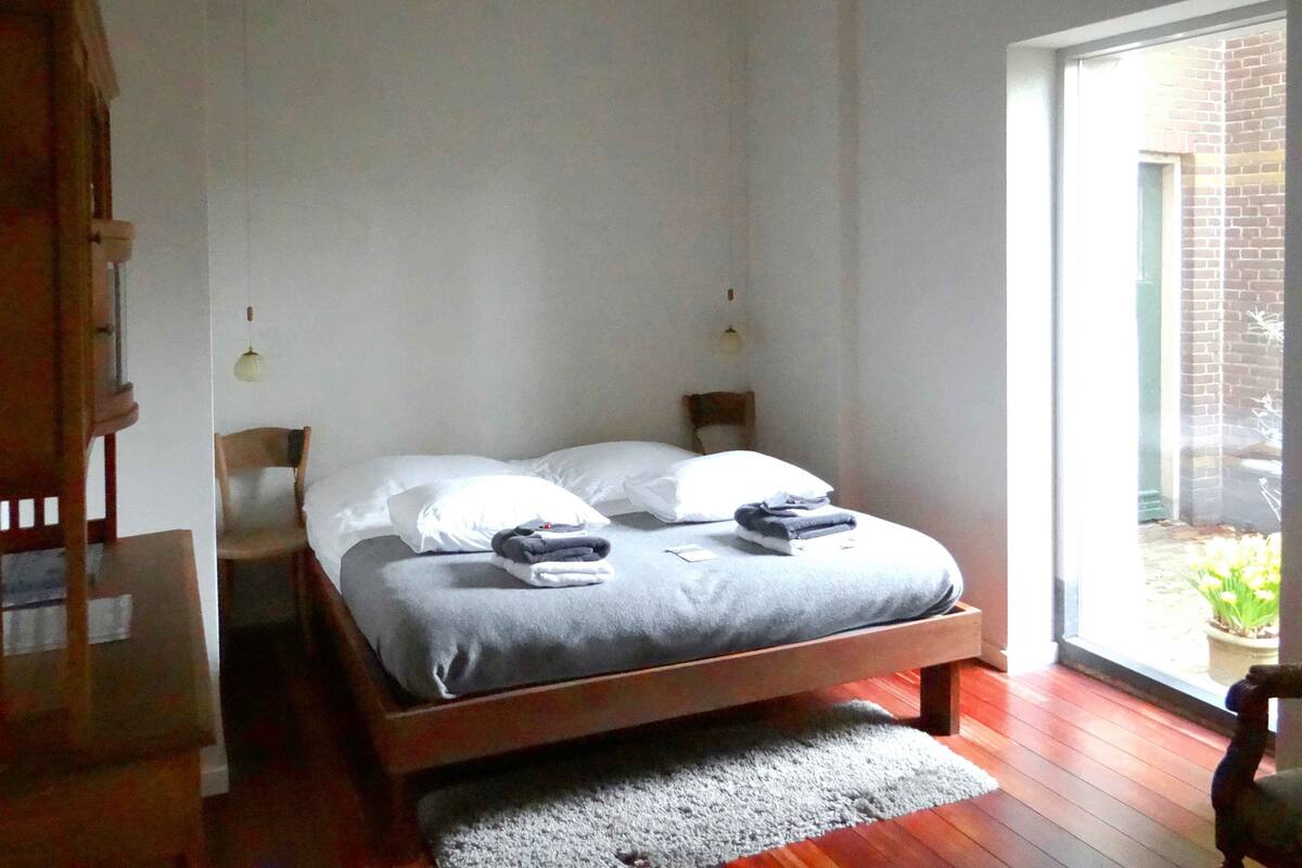 Een slaapkamer met een houten bed, twee kussens, een grijze deken en een kleed.