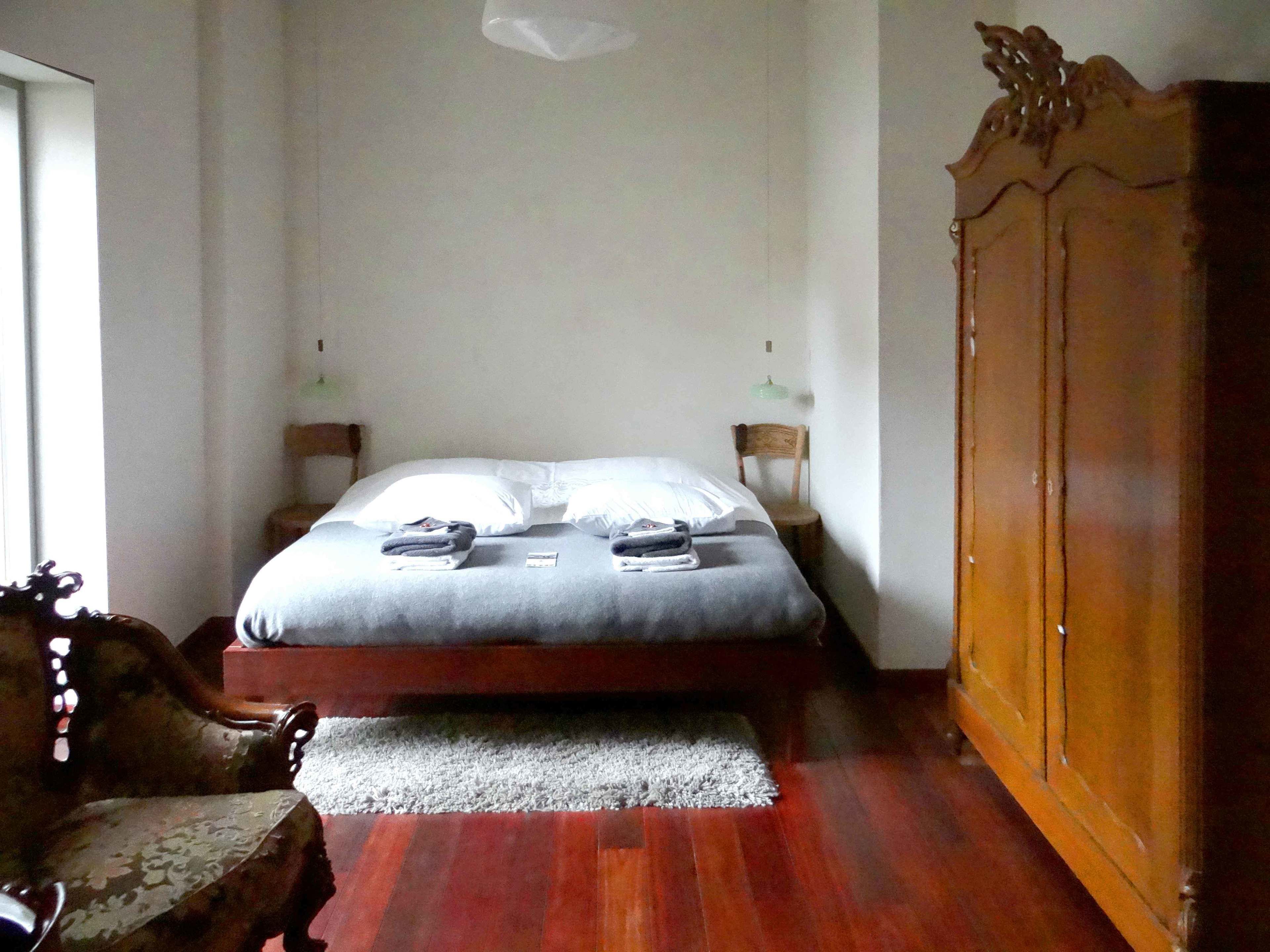 A bedroom with a bed, a wooden wardrobe, a chair, and a small rug.