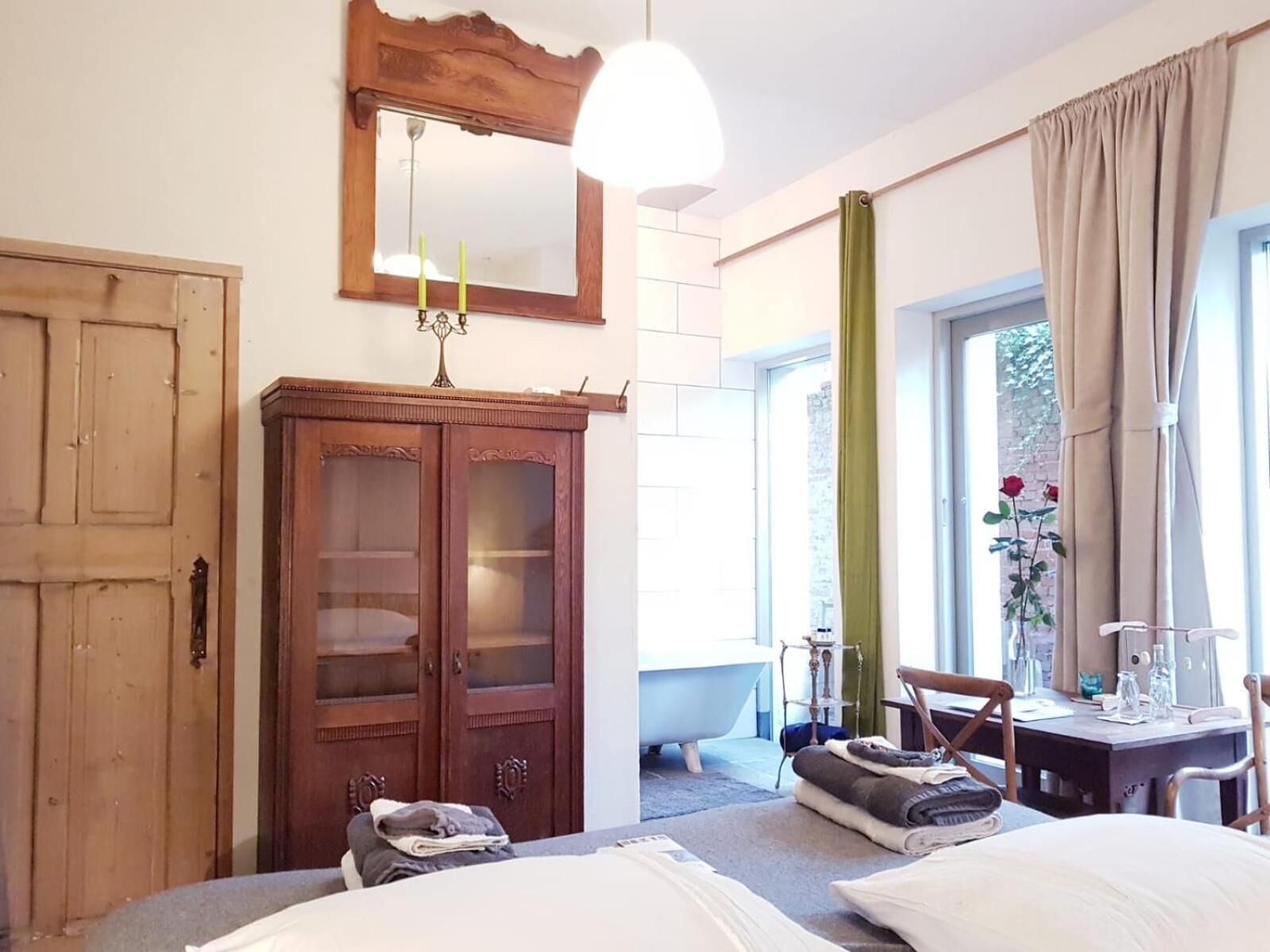 Een slaapkamer met een houten garderobe, een bed met kussens, een bureau met stoel, een raam met gordijnen en een hanglamp.