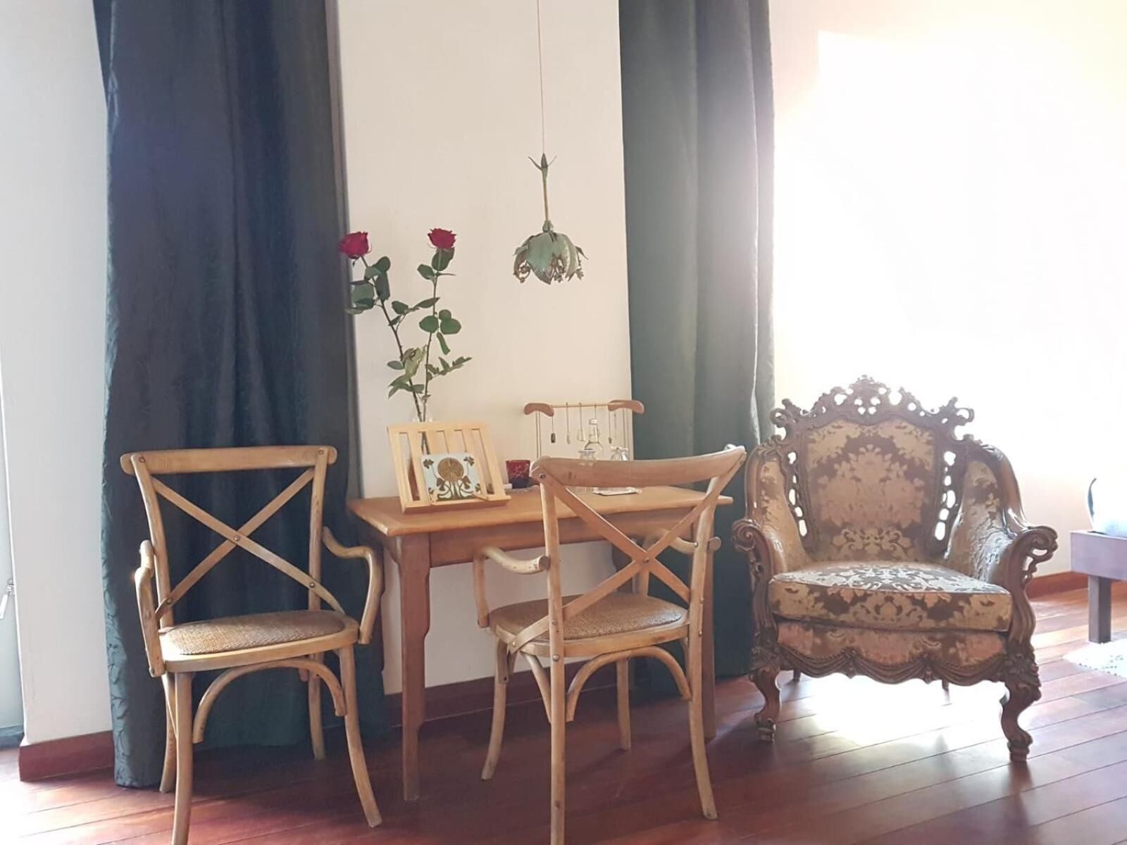 Une pièce avec une table en bois, deux chaises, un fauteuil décoratif et une plante suspendue ornée de fleurs rouges.
