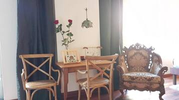 Une pièce avec une table en bois, deux chaises, un fauteuil décoratif et une plante suspendue ornée de fleurs rouges.