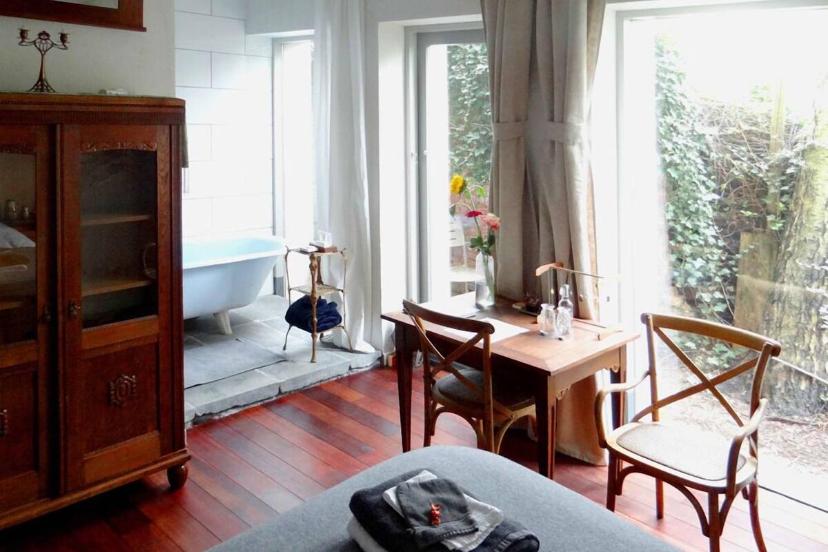 Een badkamer met een vrijstaand bad, een houten kast en een tafel met stoelen.