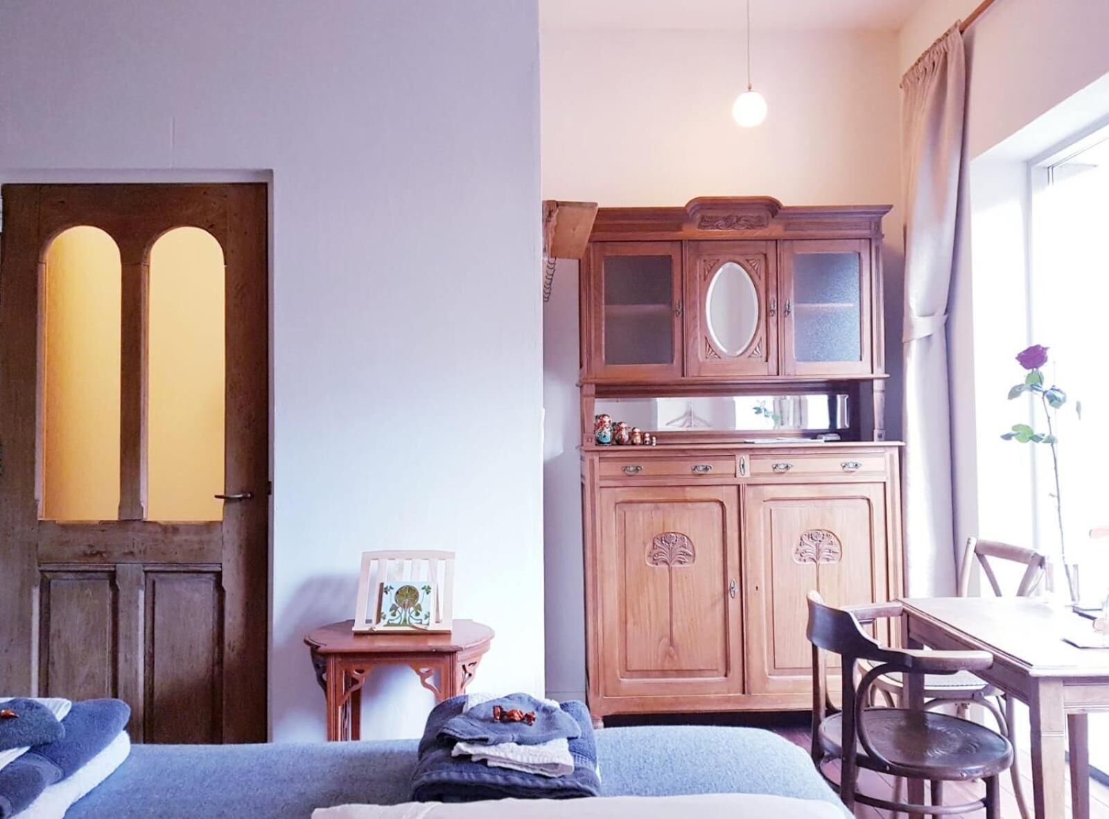 Een slaapkamer met een bed, een houten kast met spiegel, een klein tafeltje met een fotolijst en een raam met een bloem.