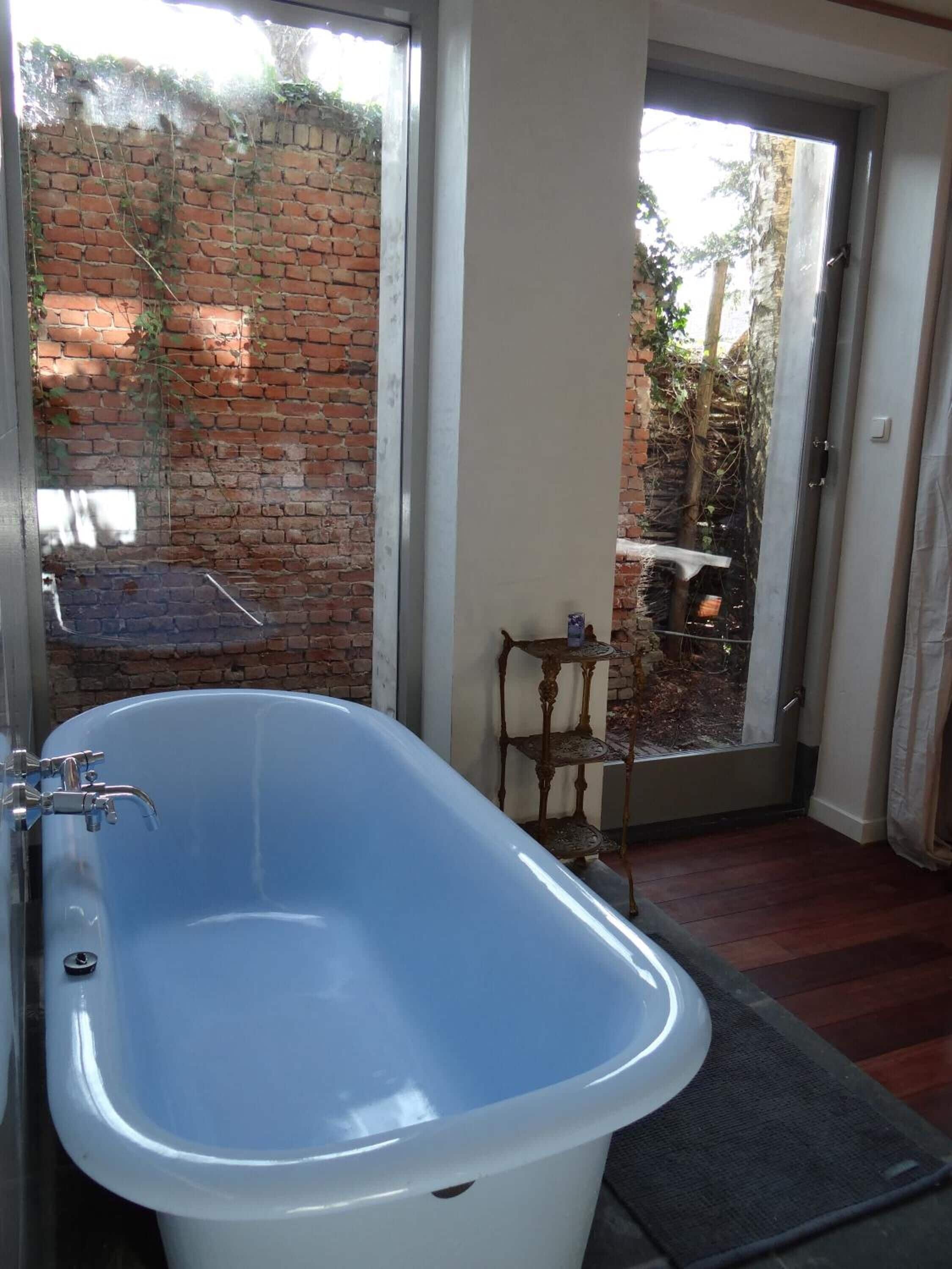A bathroom with a freestanding bathtub, a glass shower enclosure, and a view of a brick wall and outdoor area.