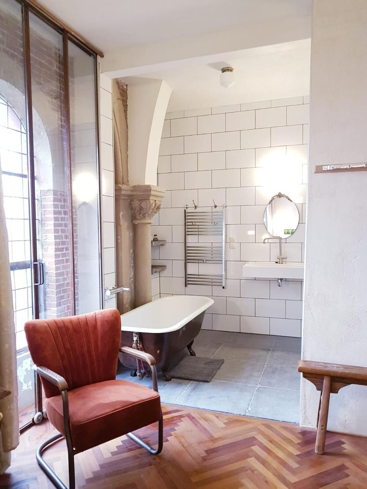 A bathroom with a bathtub, a mirror, and a red chair.