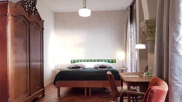 A bedroom with a bed, a wooden wardrobe, a desk with a chair, and a window with curtains.