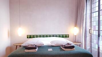 A hotel room with a bed, two bedside lamps, a window with curtains, and a wall with a green decorative panel.