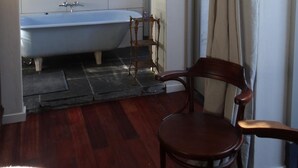 Een badkamer met een witte betegelde muur, een vrijstaand bad, een houten stoel en een raam met gordijnen.