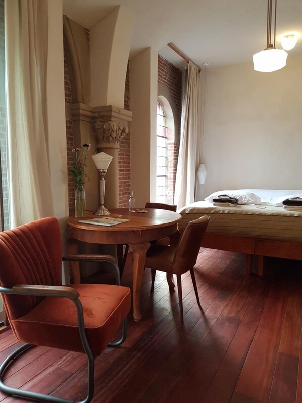 A cozy room with a wooden dining table, two chairs, a bed with a white duvet, and a brick wall. - SintAnna B&B PetitHotel (Yerseke)