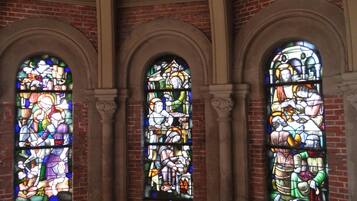Three arched stained glass windows with intricate designs, set in a brick wall with stone arches.