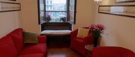 A room with a wooden floor, red sofas, a bench, and a window with a view of buildings.