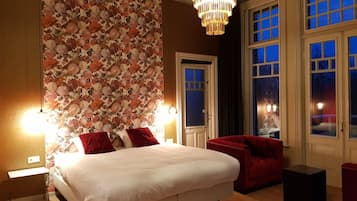 Un dormitorio con una cama grande, un sofá rojo, una araña de cristal y un papel pintado con motivos florales.