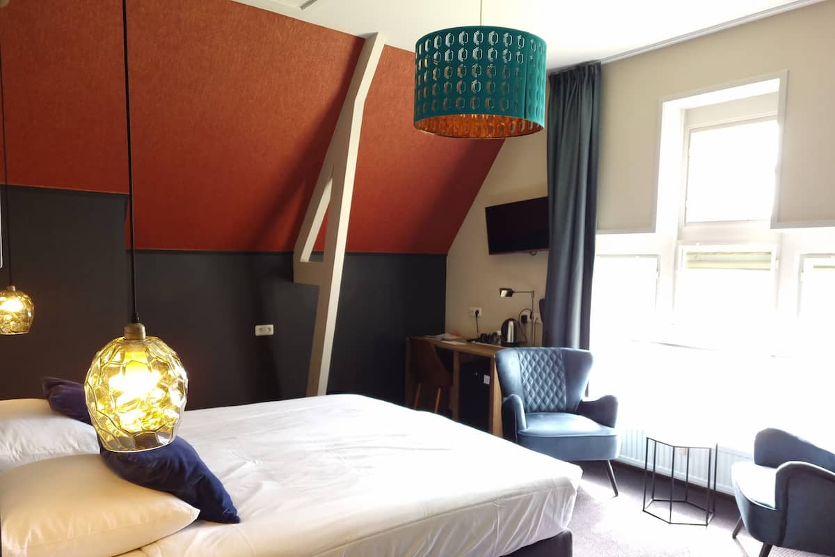 A modern hotel room with a large bed, a desk, and a chair.