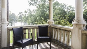 A balcony with two wicker chairs, a stone balustrade, and a view of trees and greenery. - Rijksmonument Hotel de Sprenck (Middelburg)