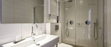 Un baño moderno con lavamanos blanco, espejo y cabina de ducha con paredes de vidrio.