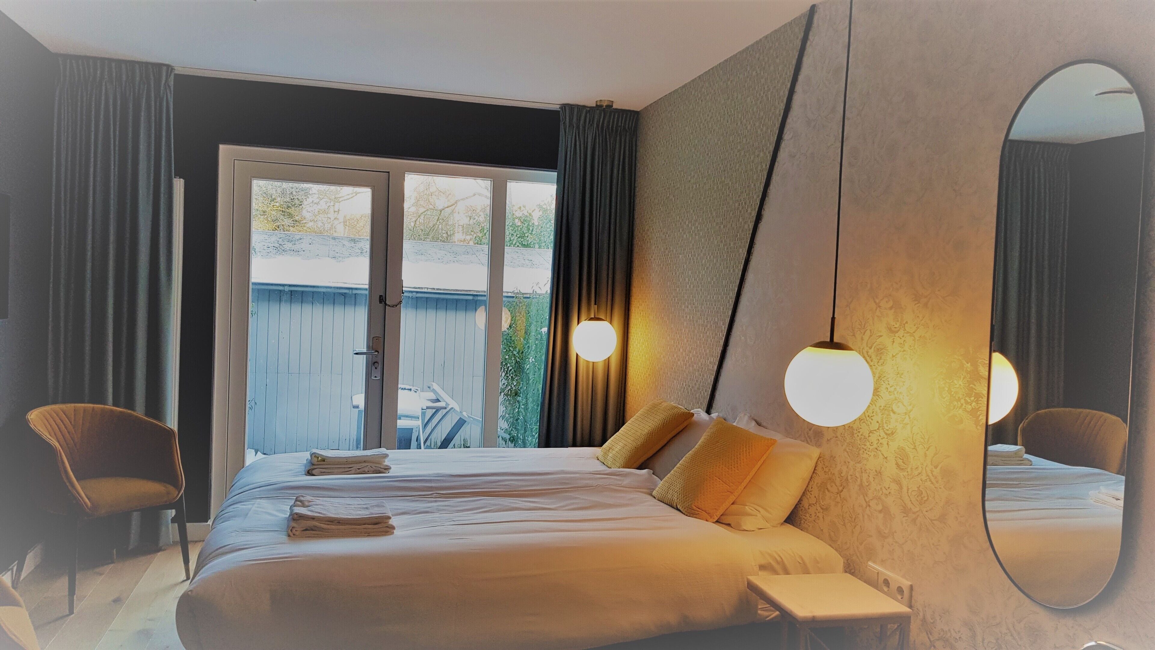 A bedroom with a large bed, two bedside tables, a mirror, and a view of the outdoors.