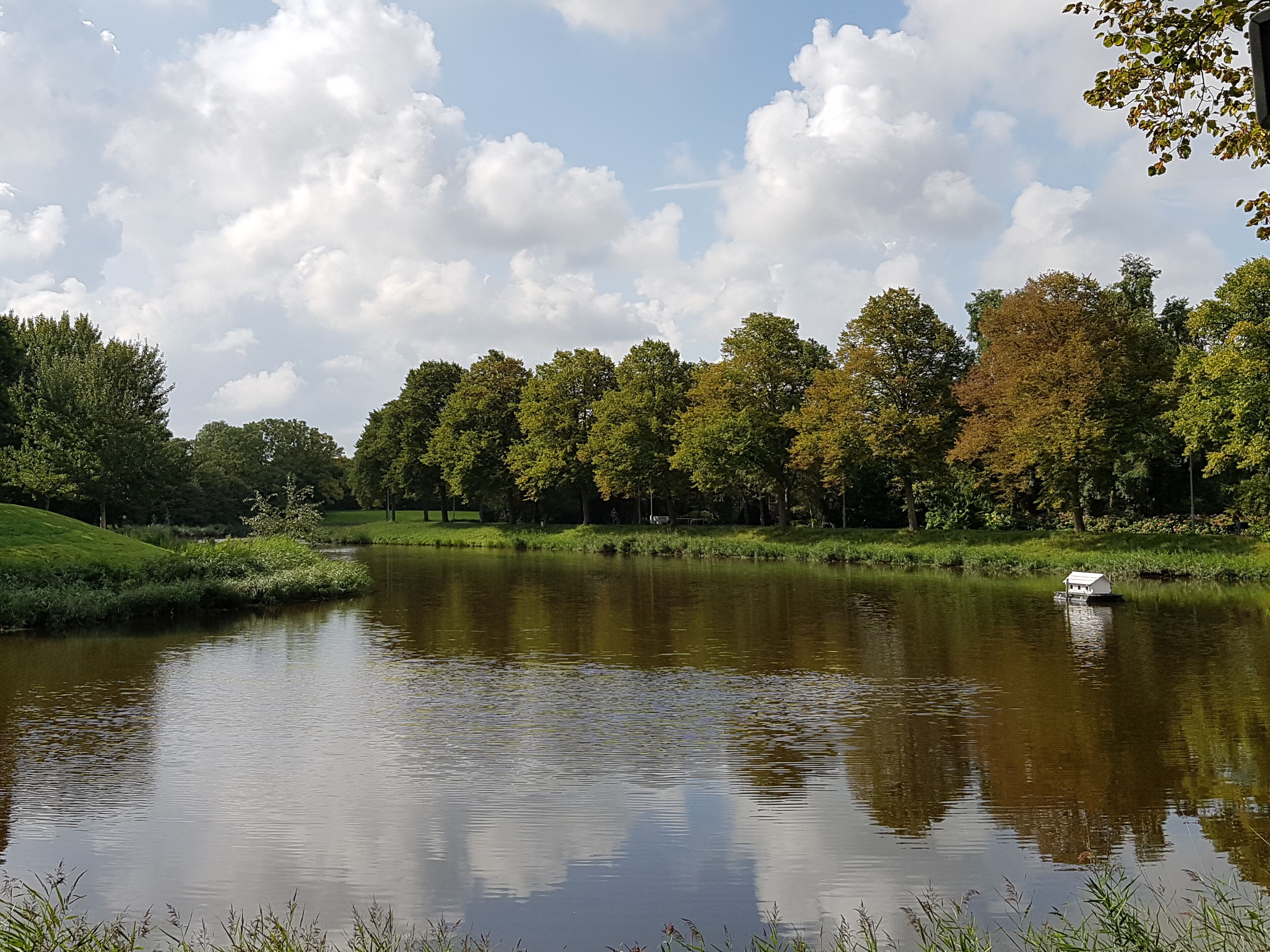 A calm lake with a small houseboat on the water, surrounded by lush greenery and trees.