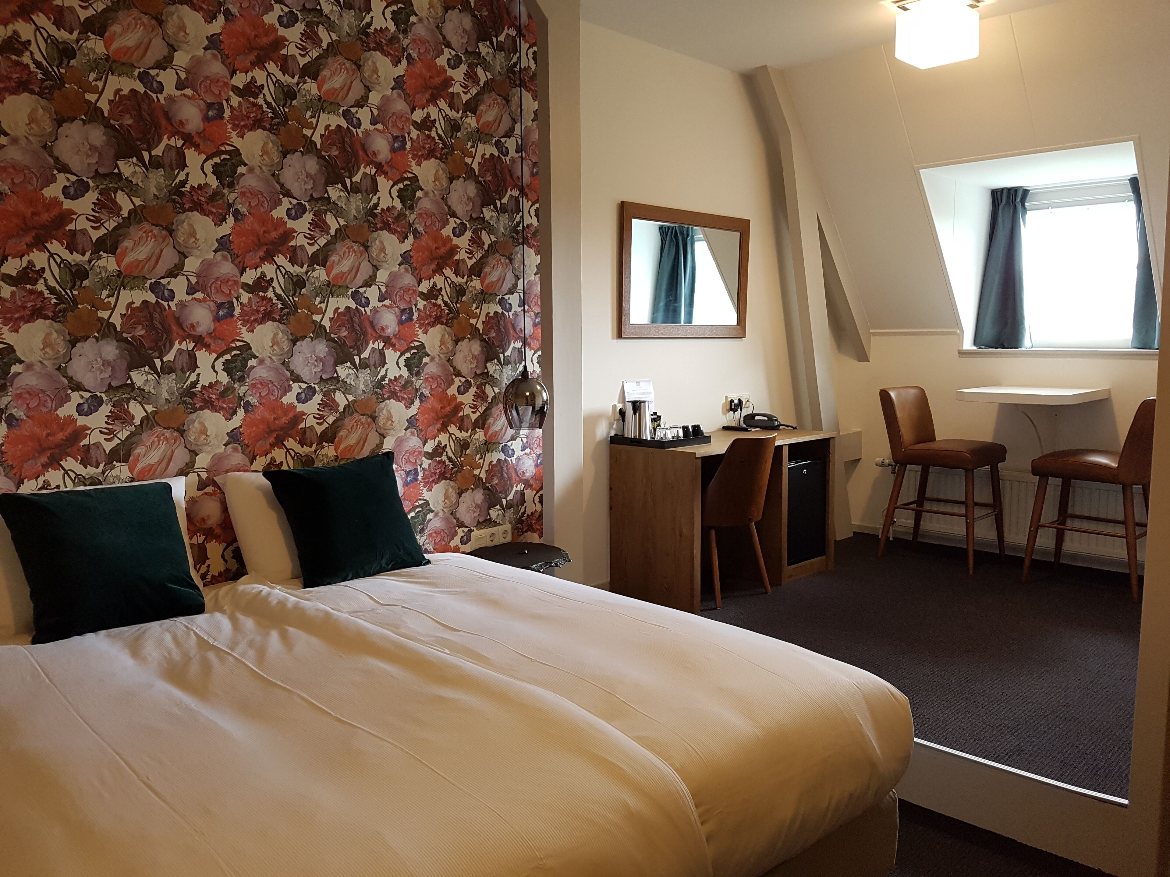 Habitación de hotel con cama, escritorio, dos sillas, una mesita y una ventana con cortinas.