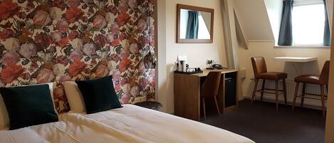 A hotel room with a bed, a desk, two chairs, a small table, and a window with curtains.