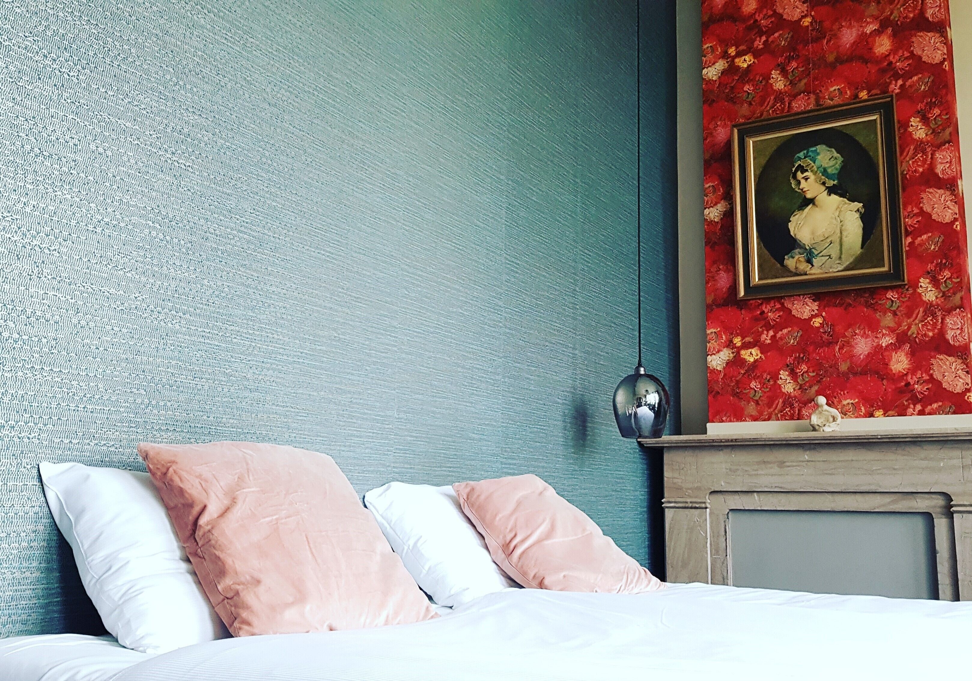 A bedroom with a bed, pillows, a wall with a textured pattern, a fireplace, and a framed picture on the wall.