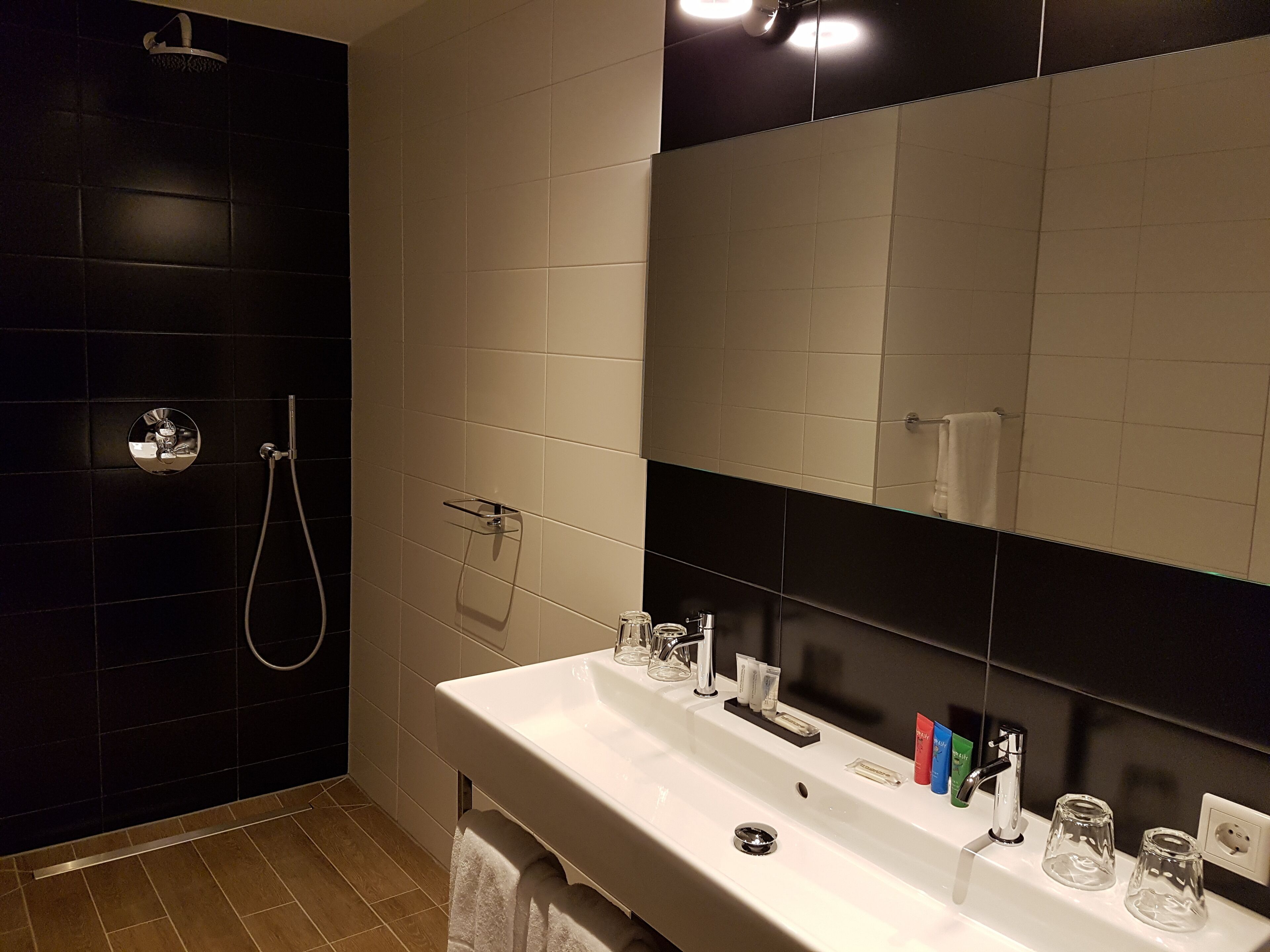 A modern bathroom with a large mirror, white sink, and black tiled walls.