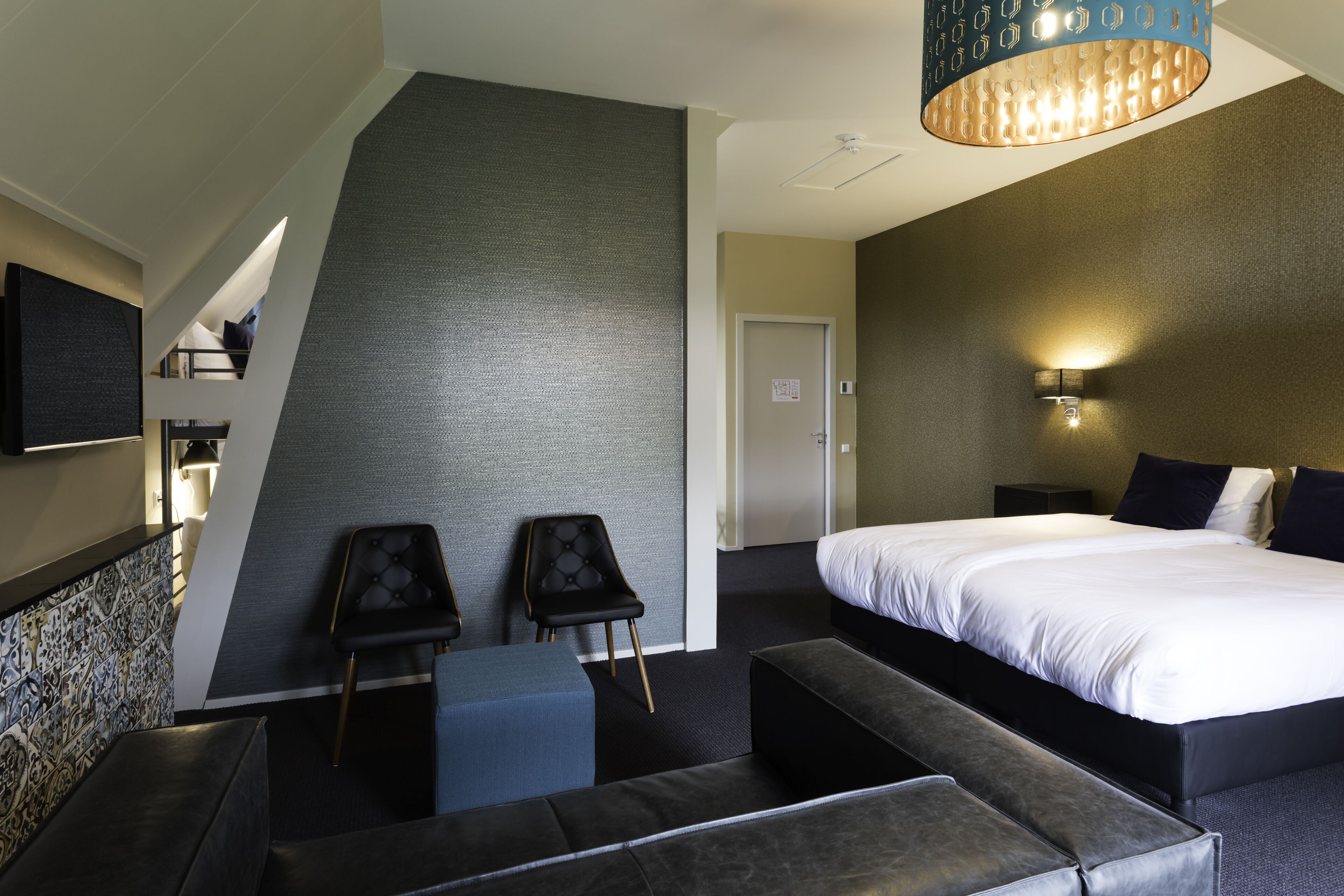 Une chambre d’hôtel moderne dotée d’un grand lit, d’un coin salon avec deux fauteuils, d’une petite table et d’un téléviseur fixé au mur.
