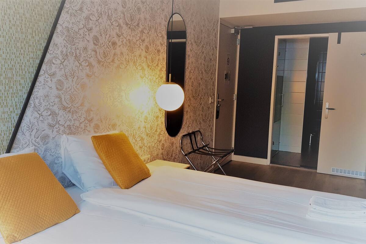 A hotel room with a bed, two pillows, a chair, a mirror, and a door.