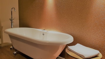 Una bañera tipo pata de león en un baño con pared texturizada y una pequeña mesa redonda con una toalla.