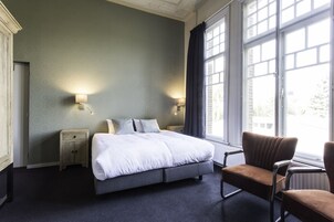 Habitaci ón de hotel con una cama grande, dos lámparas de noche, una silla y vistas al exterior a través de amplias ventanas.