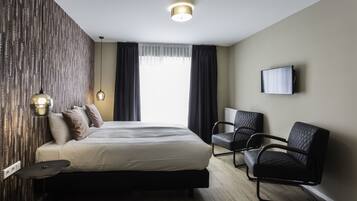 A modern hotel room with a large bed, two black chairs, a flat-screen TV, and a patterned wall.