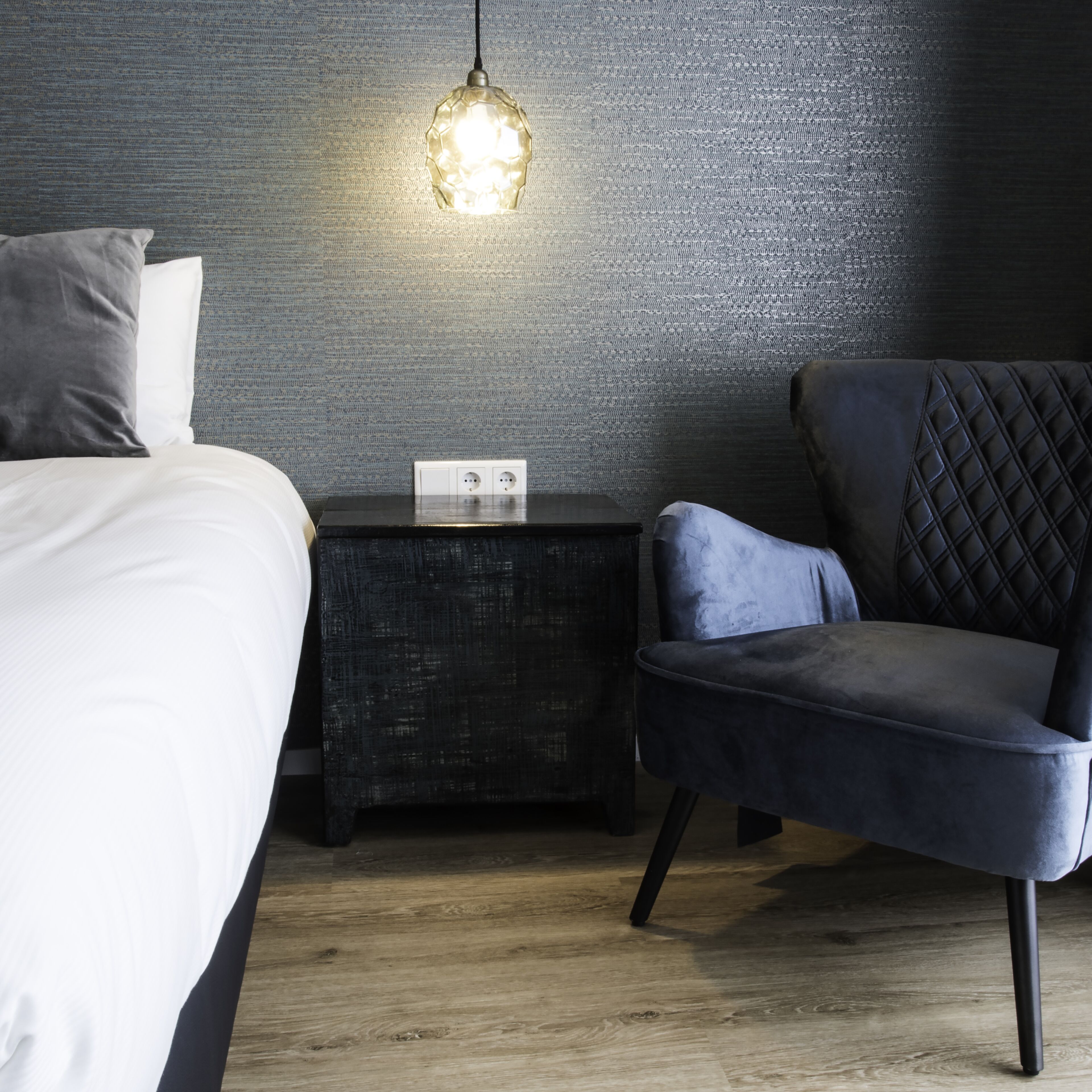 A modern bedroom with a bed, a nightstand, a chair, and a textured wall.