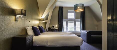 Habitación de hotel moderna con una cama grande, un escritorio, una silla, una lámpara y una ventana con cortinas.