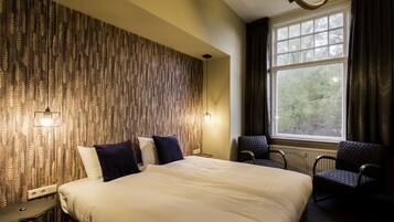 A hotel room with a large bed, two chairs, a window with curtains, and a patterned wall.