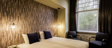 A hotel room with a large bed, two chairs, a window with curtains, and a patterned wall.