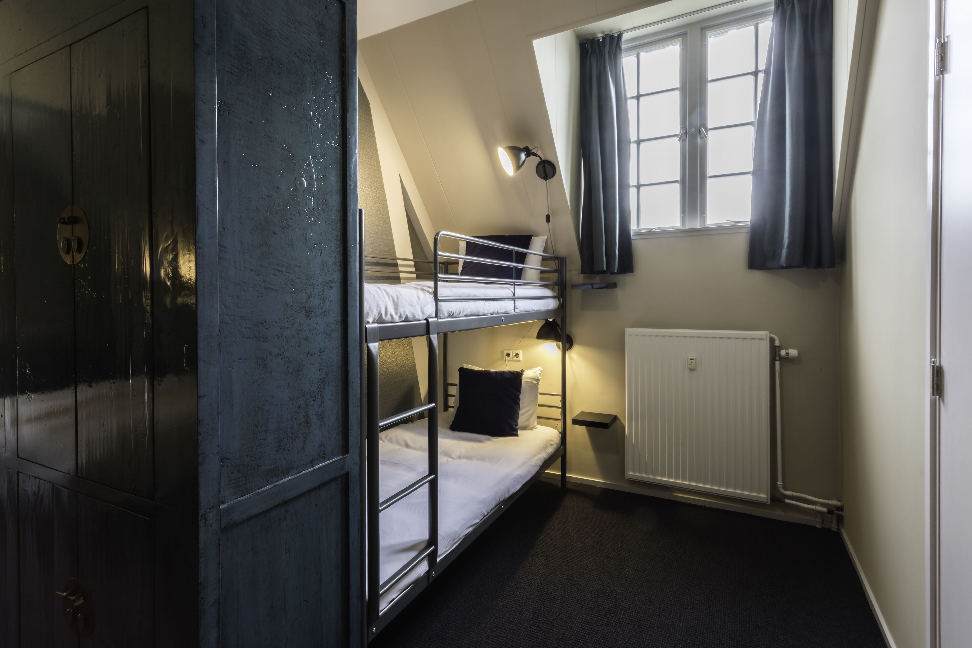 A bunk room with a window, a radiator, and a wardrobe.