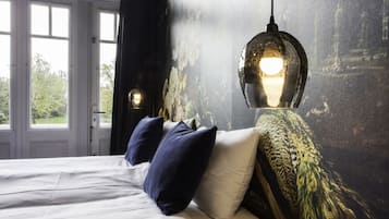 Un dormitorio con cama, dos almohadas, un muro con estampado floral y una ventana.