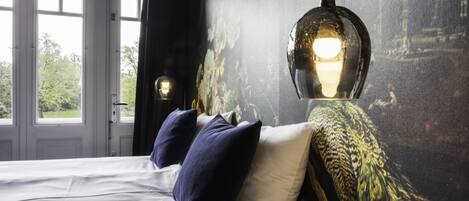 Un dormitorio con cama, dos almohadas, un muro con estampado floral y una ventana.