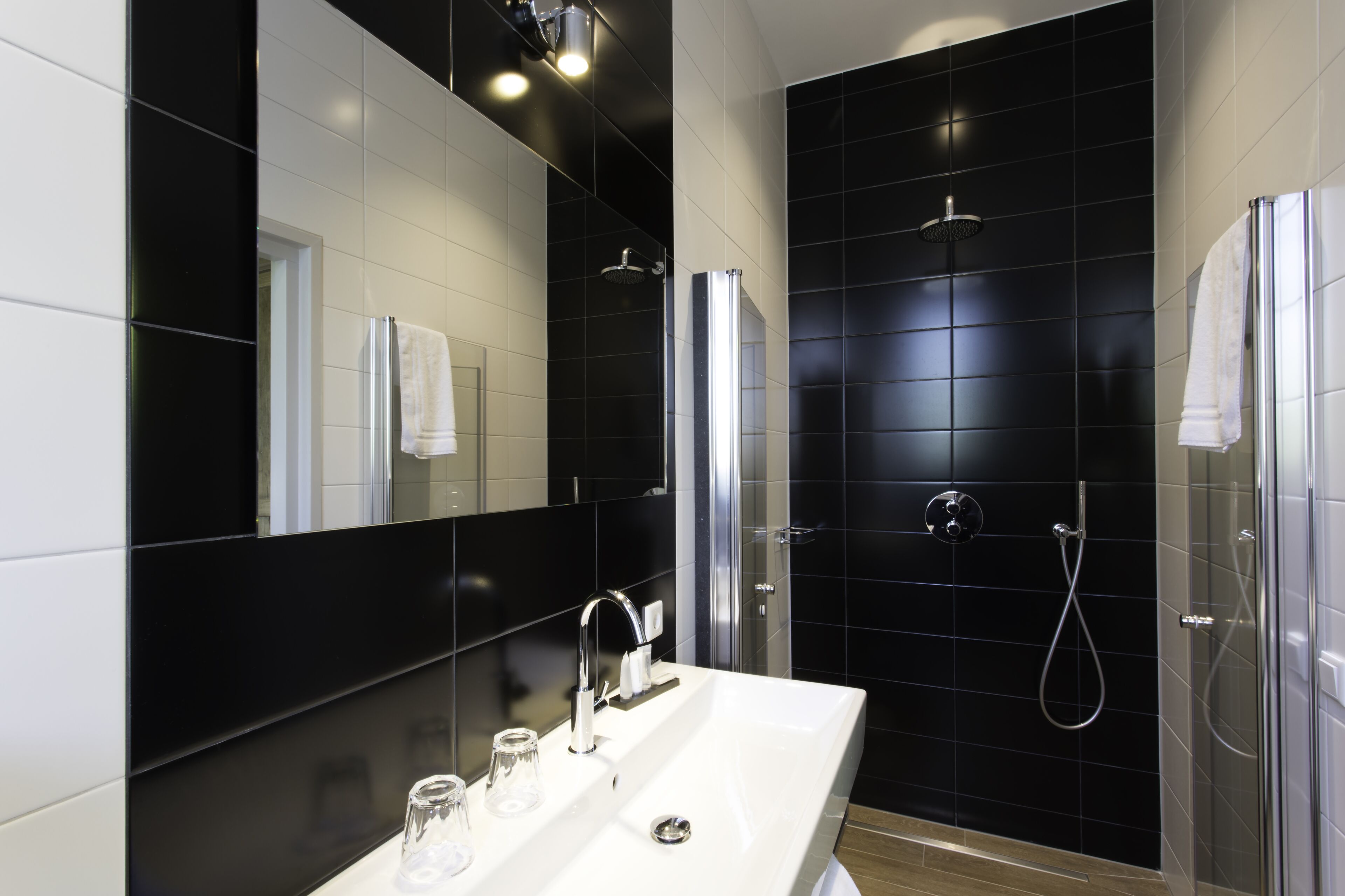 A modern bathroom with a white sink, a large mirror, and a black tiled shower area.