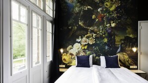 A bedroom with a large bed, a window, and a mural on the wall. - Rijksmonument Hotel de Sprenck (Middelburg)