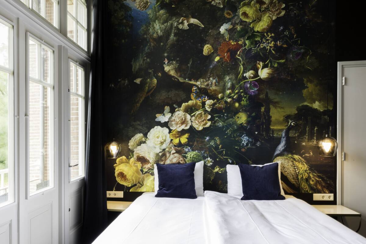 A bedroom with a large bed, a window, and a mural on the wall.