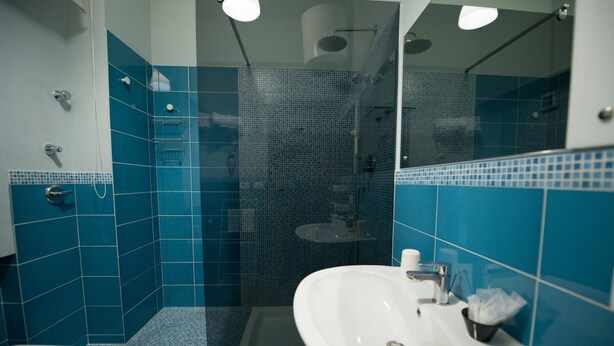 A bathroom with a white sink, blue tiles, and a glass-enclosed shower area. - Sale e Sabbia B&B (Trapani)