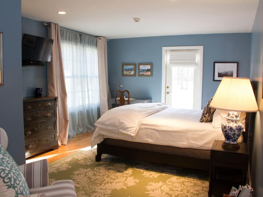 A bedroom with a bed, dresser, lamp, and artwork on the wall.
