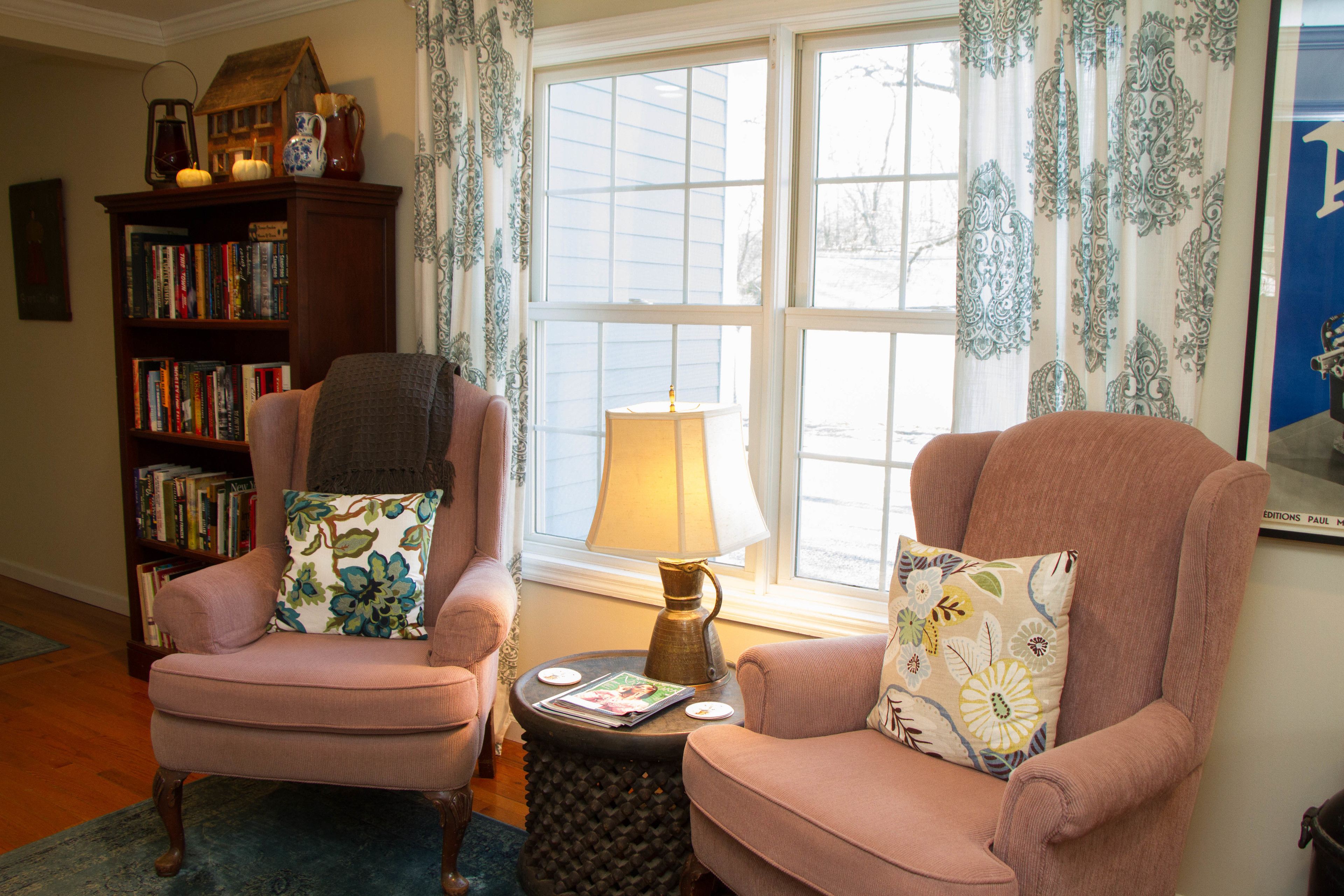 A cozy living room with two armchairs, a bookshelf, and a window with curtains.