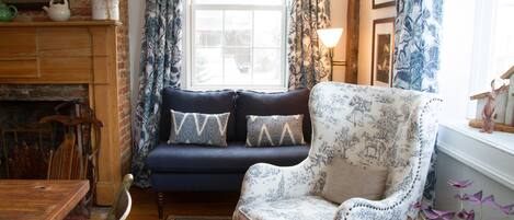 Una sala de estar acogedora con un sofá azul oscuro, un sillón estampado y una chimenea de madera.