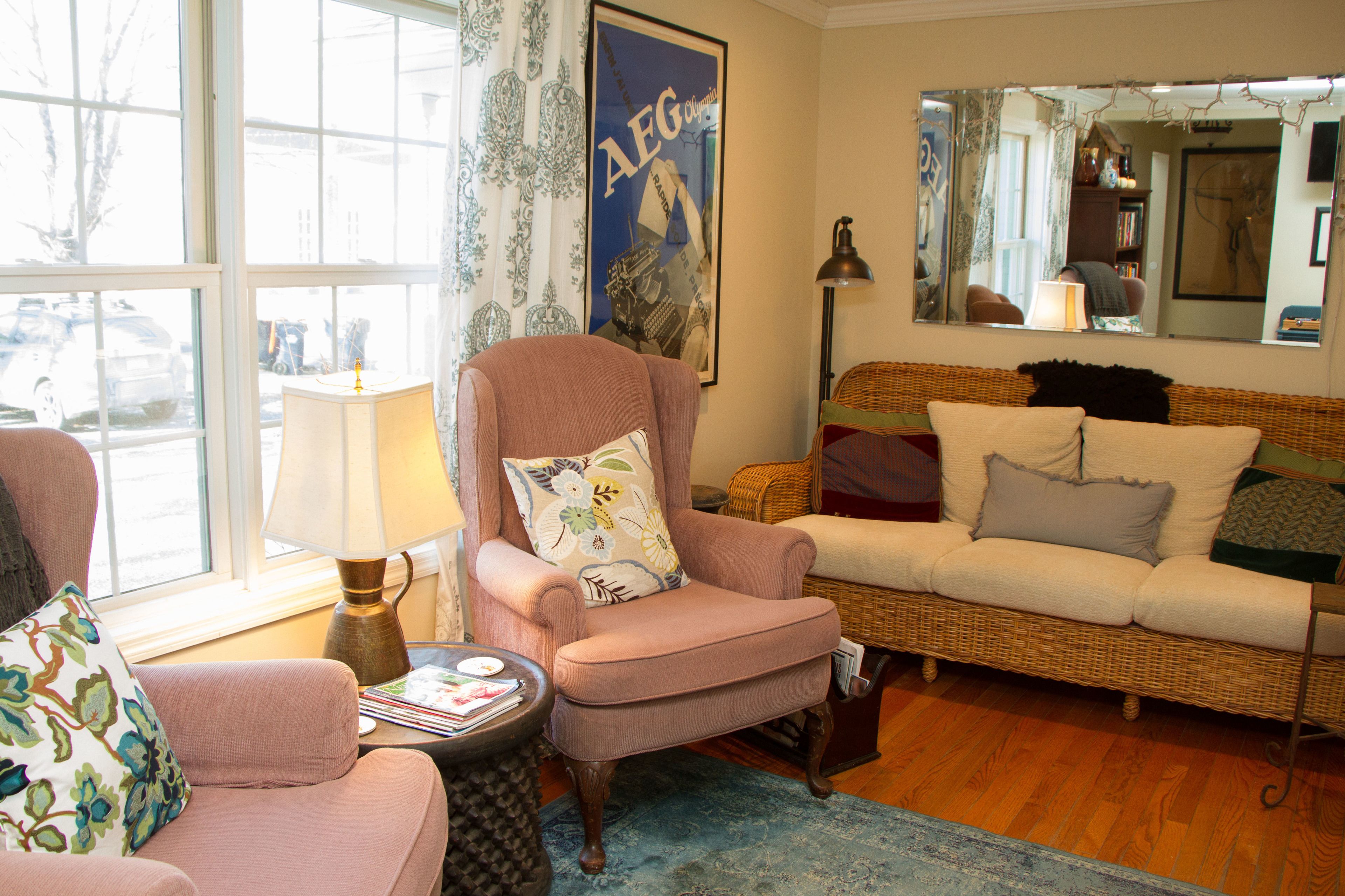 A cozy living room with a pink armchair, a wicker sofa, and a round coffee table.