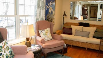 A cozy living room with a pink armchair, a wicker sofa, and a round coffee table.