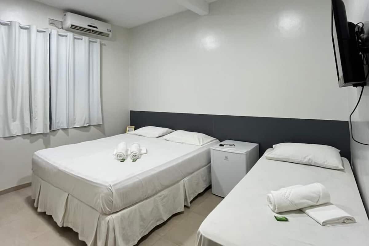 A hotel room with two beds, a TV, an air conditioning unit, and a small table.