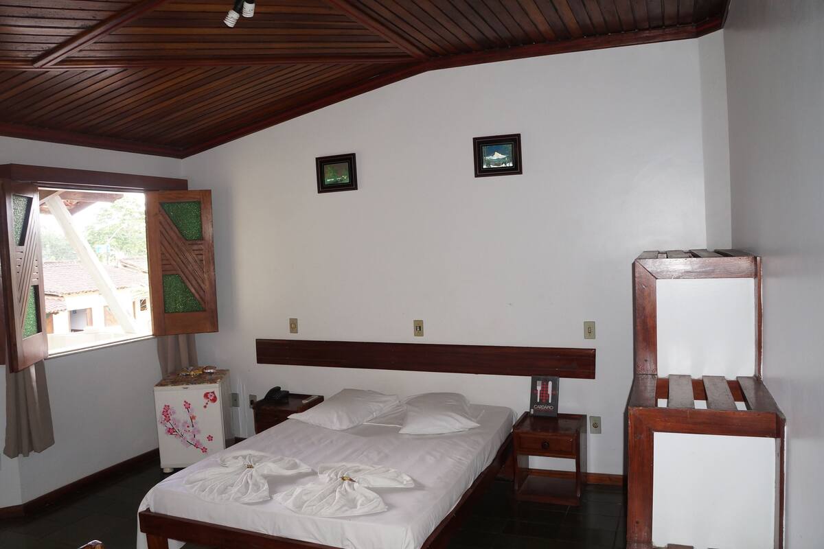 A neatly made bed with white linens, a wooden headboard, and two small framed pictures on the wall.